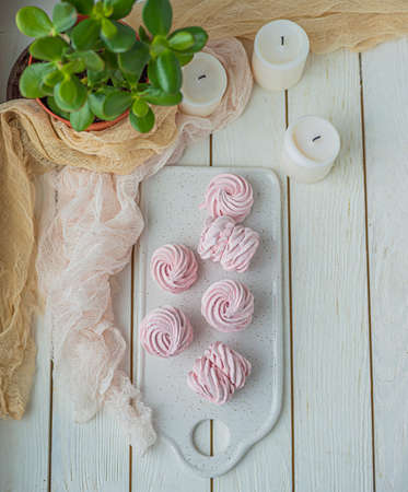 homemade Marshmallow zephyr on a white plate with candles and room tree on a light wooden table. Pink sweet homemade marshmallow. Colorful meringues on a white background. dessert image. flat ley. The view from the topの写真素材
