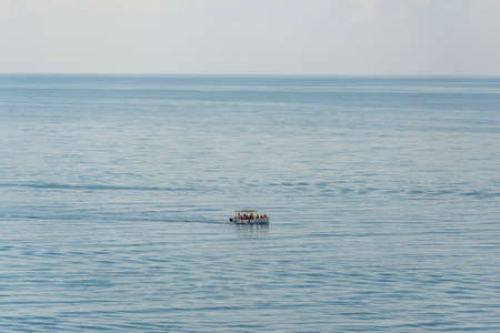Aerial view on a white floating boat with people in it in the blue black sea.