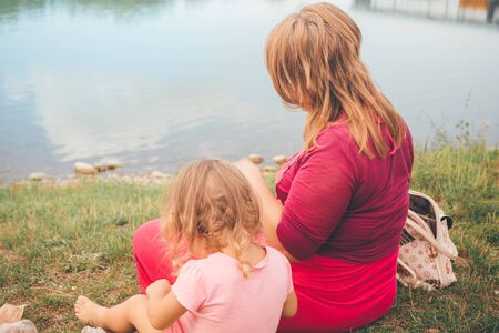 Mother and daughter sitting on the beach in a nice summer day. Concept of happy family outdoors.の写真素材
