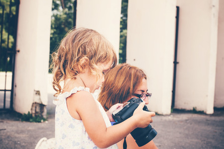Little girl holding a camera and taking pictures. Little baby girl professional photographer outdoors. Concept development and training success.の写真素材