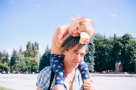 The father carries his daughter on his shoulders. Walking outdoors little curly girl and her father. The concept of a happy family, a happy relationship.の写真素材