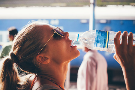 Beautiful girl having fun drinking water outdoors, close-up portrait. A girl in India traditionally drinks clean water from a bottle. Concept - water, ecology, thirst.の写真素材