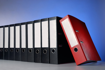 A red folder in front of a row of black folders の写真素材