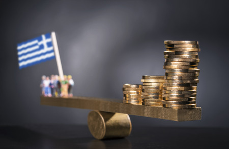 Seesaw with coins on one side and a group of people with the Greek flag on the other side.の写真素材