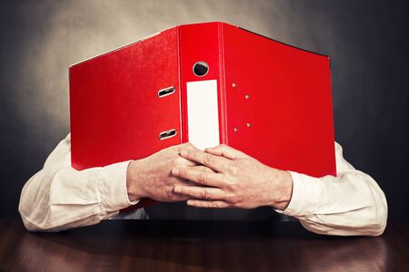 An employee hides his face behind a red file folder.の写真素材