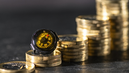 Needle of a compass points to rising stacks of coins