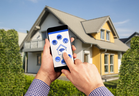 A remote control with icons for operating a smart home with house in the backgroundの写真素材