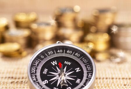 Several stacks of coins with a compass in the foreground