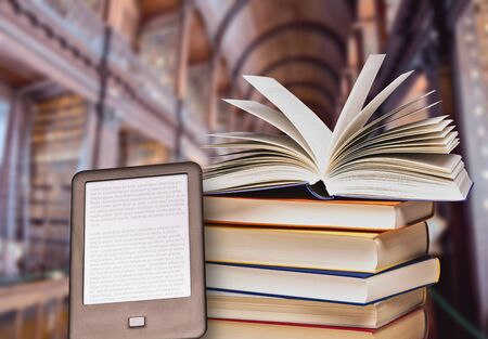 Stack of books with an open book and e-book reader in a large libraryの写真素材