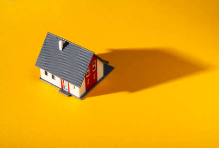 A small model house on a warm yellow ground casts a long shadowの写真素材