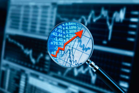 Magnifying glass with red arrow and financial data and monitor in backgroundの写真素材