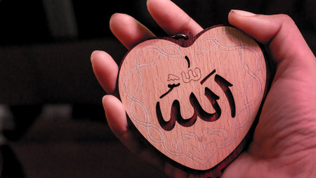 Muslim woman hand holding heart(Love) shaped tag written in Arabic "Allah" English meaning of God.の写真素材