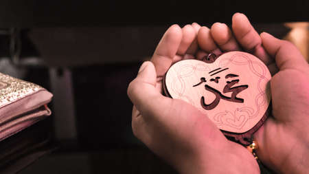 Muslim woman hands holding heart(Love) shaped tag written in Arabic "Muhammad" English meaning of Prophet Mohamed.の写真素材