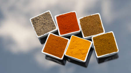 Colorful spices for cooking: Chilli, turmeric,pepper, curry powder etc. Indian spices in ceramic bowl. On glass table with sky shadow outdoor background. Top view.の写真素材