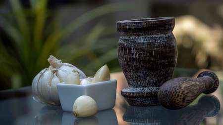 Fresh garlic with wooden mortar on modern glass table on nature backgroundの写真素材