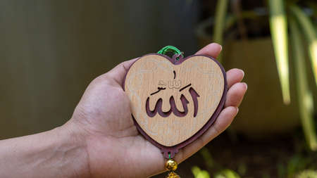Hand holding heart(Love) shaped tag written in Arabic "Allah" English meaning of God.の写真素材