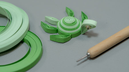 Green paper stripes making turtles on grey background with wooden needle and quilling paper stripes.の写真素材