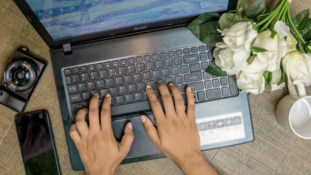 Female hands typing on a laptop keyboard with a bouquet of white rosesの写真素材