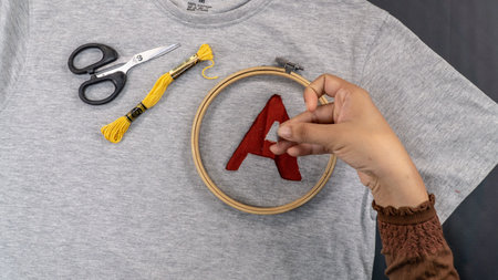 Handmade embroidered red letter A on a gray t-shirt. Top view.
