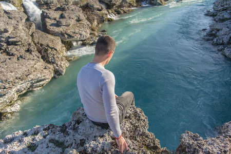 Fit guy sitting on edge of rock above the riverの写真素材