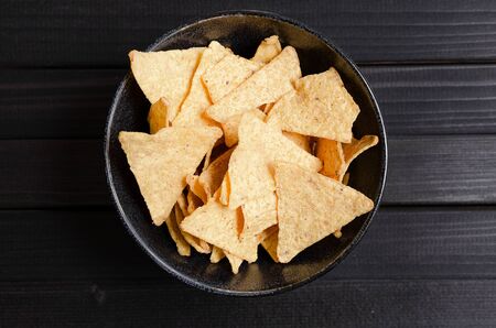 Mexican nachos with sauces tomato ketchup, cheese and guacamole in wooden bowl on dark background, top view, copy space. Delicious salty corn chips triangular nachos snack for partyの写真素材