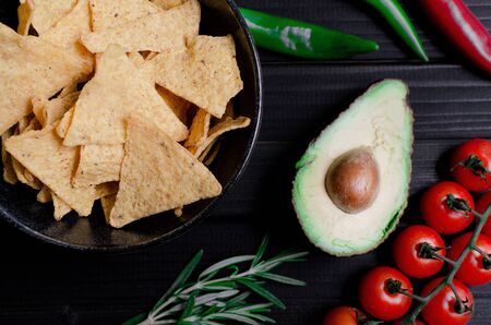 Mexican nachos with sauces tomato ketchup, cheese and guacamole in wooden bowl on dark background, top view, copy space. Delicious salty corn chips triangular nachos snack for partyの写真素材