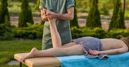 Male therapist giving foot massage massage to athlete patient on bed in beautiful yard for sports physical therapy concept. selective focusの写真素材
