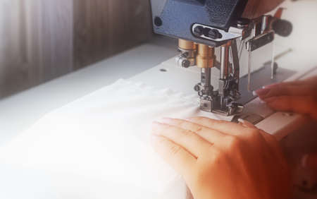 A woman sews on an industrial flat-seam sewing machine. Hands close-up. Soft focus