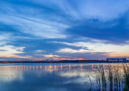 Lake at sunset. In the background there are lights and a damの写真素材