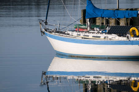 Sailboat reflection docked at a small harbor with morning lightの写真素材