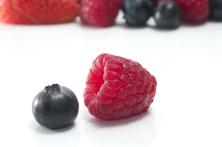 Selective focus on a single blueberry and raspberry isolated on white with more berries in the...