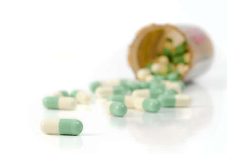 Selective focus on the foreground capsules spilled out of the pill bottle onto the white backgroundの写真素材