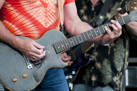 Two rock and rollers at a music festival with selective focus on the forground hands strumming the guitarの写真素材