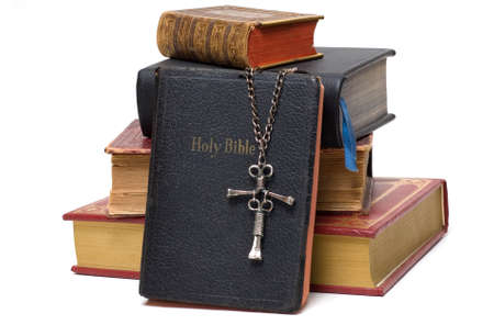 Stack of religious books with a unique nail cross resting on an old leather bible.