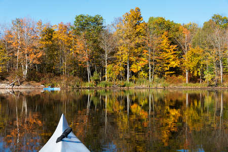 Woman taking photographs from her kayak in October with vibrant tree color reflecting on the tranquil lakeの写真素材