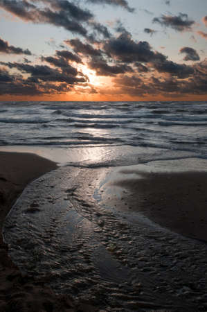 Fresh water stream flowing into the ocean at sunsetの写真素材