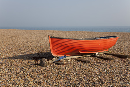 Small orange fishing or rowing boat on shingle beach,Brighton, Englandの写真素材