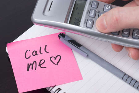 Phone on a spiral notebook with pink postit note saying CALL ME. Heart on postit. Concept for office romance or lifestyle.の写真素材