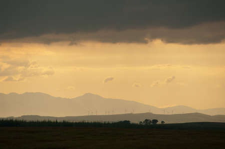 Sunset over turbines as clouds darken. Could be concept for weather uncertainty, worrying future or...