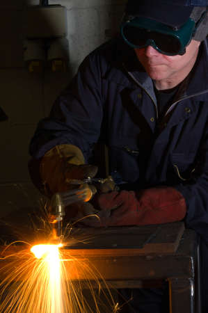 Welder uses torch to make sparks during removal of weld from metal equipment.