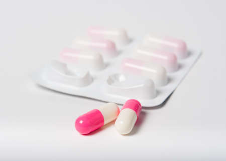 Pink pharmaceutical capsules with packaging close up on white with focus on pillsの写真素材