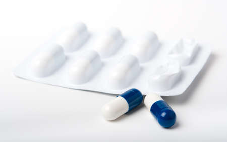 Two blue and white pharmaceutical capsules in front of blister packaging all close up on white.の写真素材