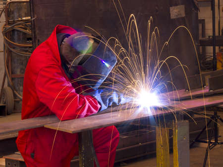 Welder in workshop manufacturing metal construction by cutting to shape using huge orange sparks