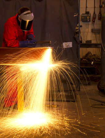 Welder in workshop manufacturing metal construction by cutting to shape using huge orange sparks