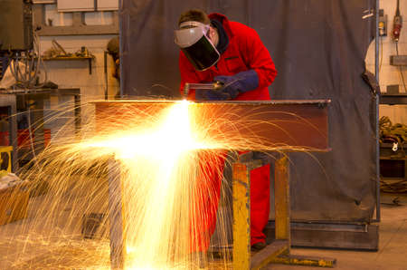 Welder in workshop manufacturing metal construction by cutting to shape using huge orange sparksの写真素材