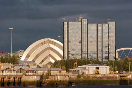 Sunlight on buildings as storm clouds gather beside River Clyde in Glasgow, Scotland, UK, Europe