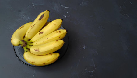 Bunch of bananas on a black plate on a dark background.の素材