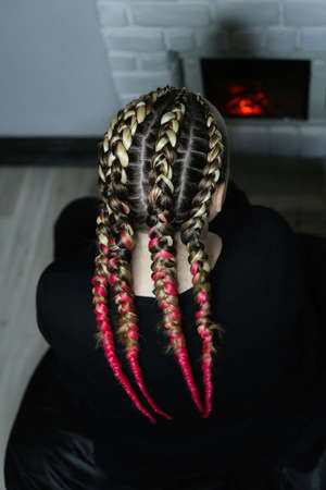 the girl is sitting near the fireplace, large braids of kanekalo