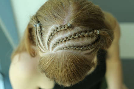 girl with a creative hairstyle from tight braids sitting on the windowsill