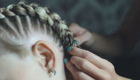 the process of braiding boxer braids on the girls head, the master makes her hair in a beauty salon, hands close-upの写真素材